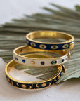 Three gold and blue patterned bracelets on a white surface with green leaves.