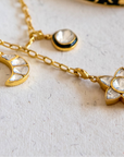 Gold necklace with star and moon charms and a black and gold bracelet on a light background