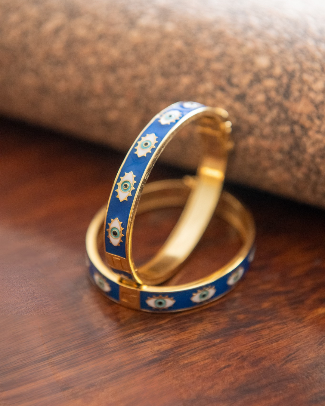 Two gold bangles with blue enamel design on a wooden surface