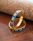 Two gold bangles with blue enamel design on a wooden surface