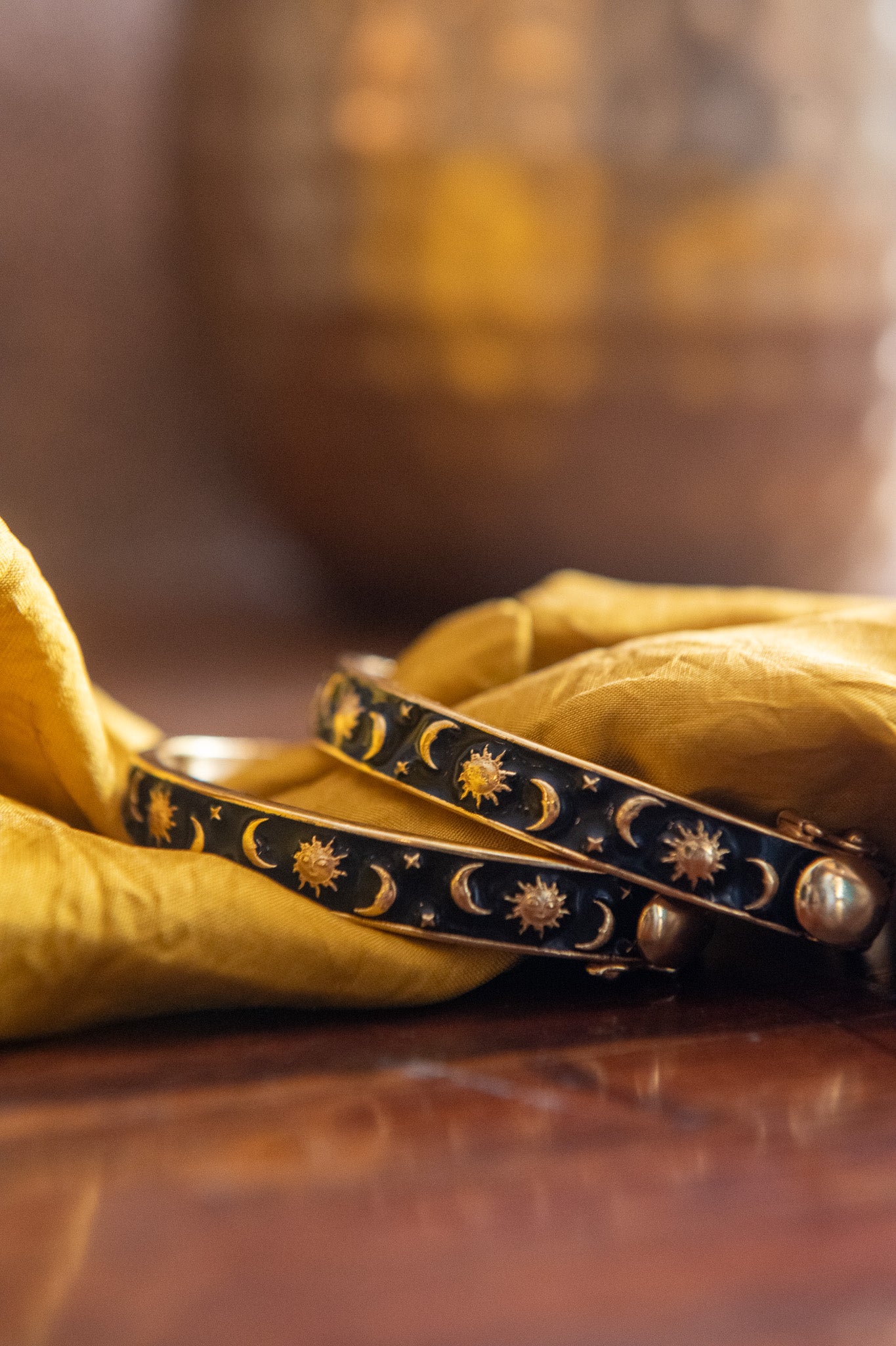 Two decorative bracelets with celestial designs on a yellow fabric background