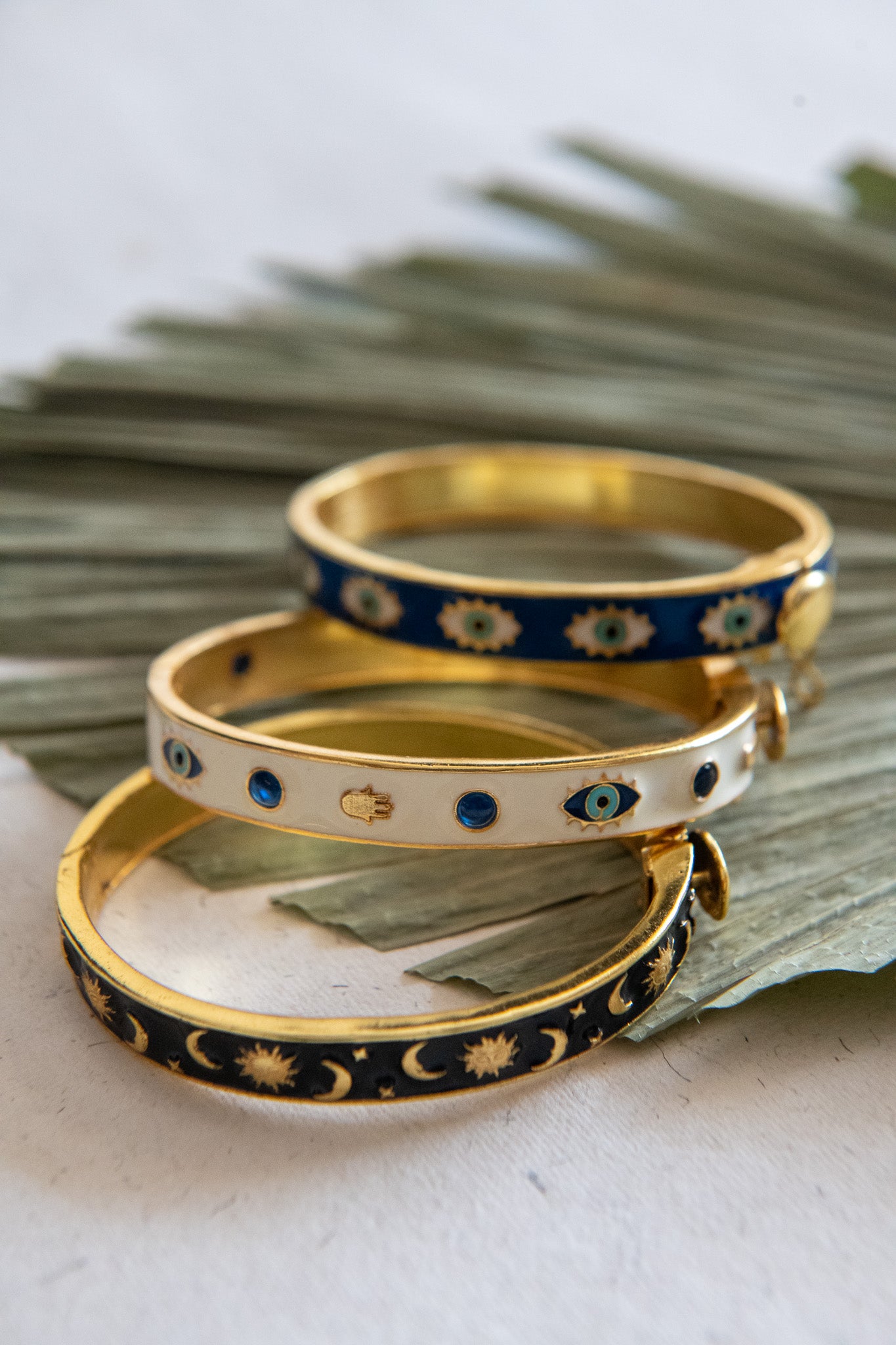 Three gold and blue patterned bracelets on a white surface with green leaves.