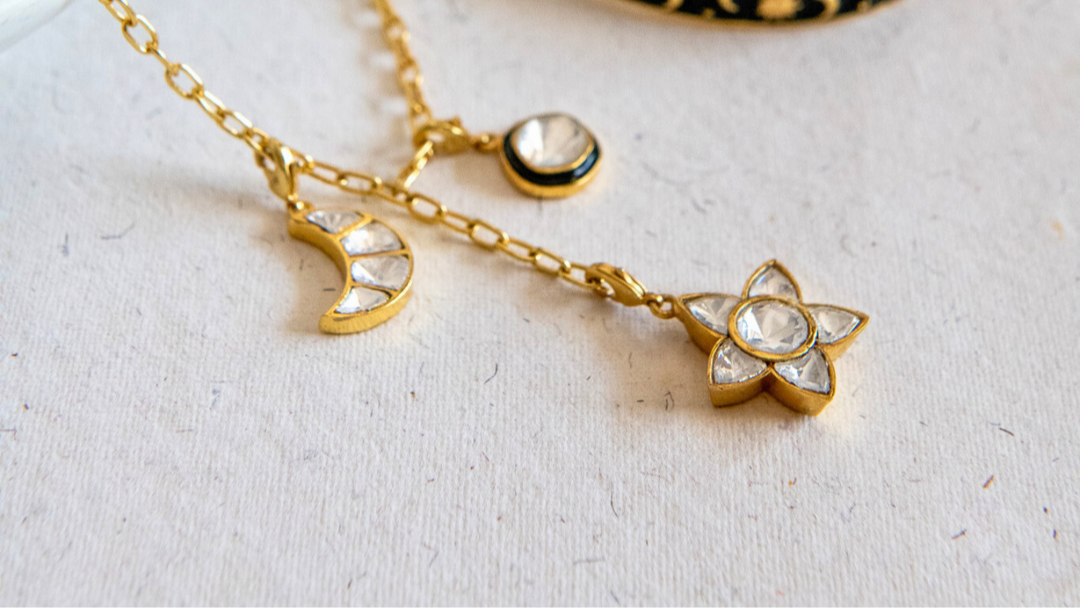 Gold necklace with star and moon charms and a black and gold bracelet on a light background