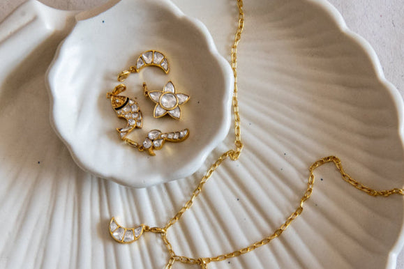 Gold necklace with star-shaped pendants on a textured white dish.