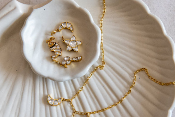 Gold necklace with star-shaped pendants on a textured white dish.